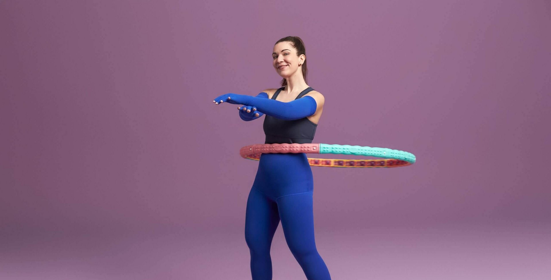 Das Bild zeigt eine Frau beim Training mit einem Hula-Hoop-Reifen. An Armen und Beinen trägt sie eine VenoTrain curaflow Versorgung in der Farbe Royal.