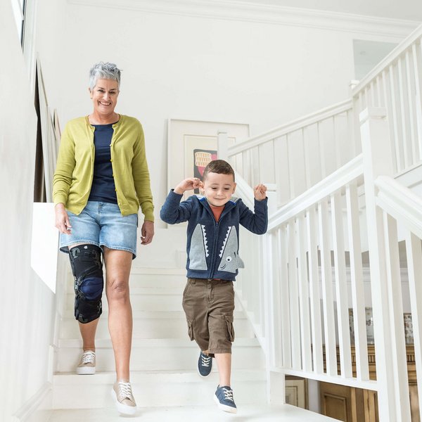 Das Bild zeigt eine Dame mit ihrem Enkel beim Herunterlaufen einer Treppe. Zur Unterstützung ihres Knies trägt die Frau eine Gonarthrose-Orthese von Bauerfeind, die GenuTrain OA.