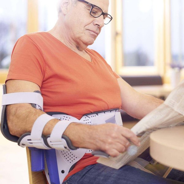 Ein Mann sitzt an einem Tisch und liest Tageszeitung. Er trägt eine OmoLoc von Bauerfeind, eine ruhigstellende Schulterorthese, an der rechten Schulter.
