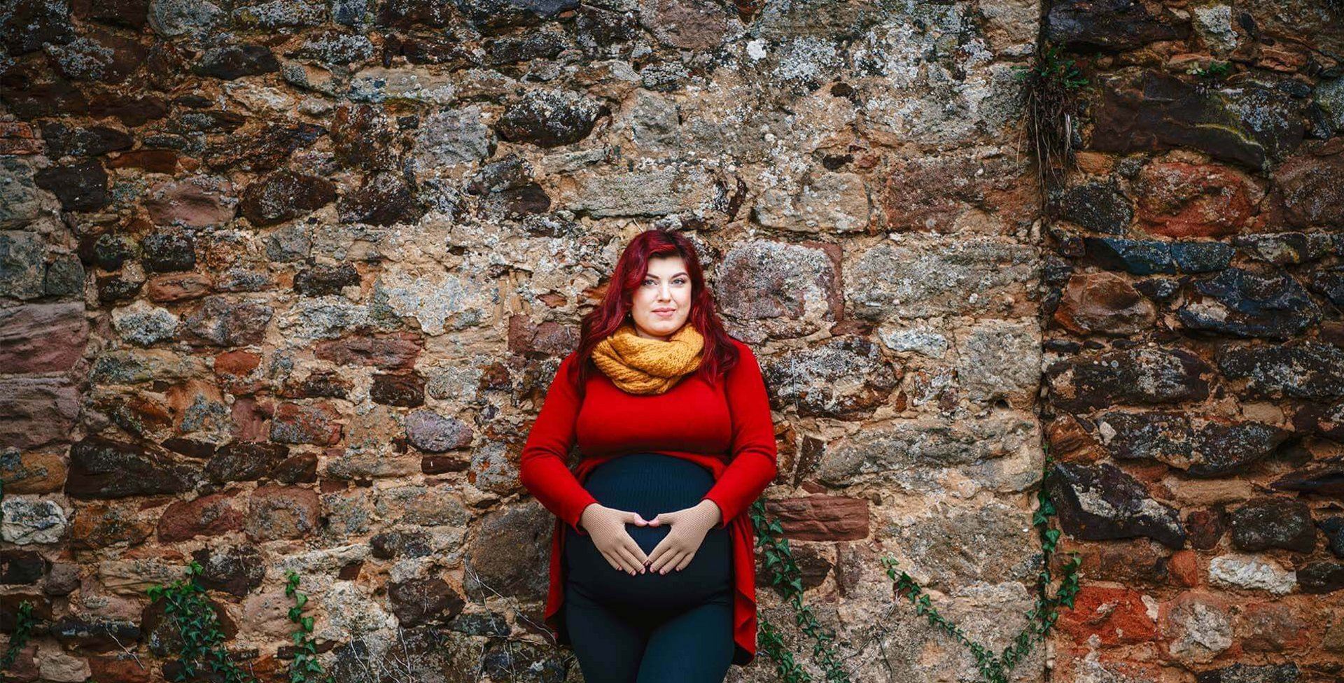 Abgebildet ist die schwangere Lipödem-Patientin Kathi Schanz, die an einer Steinmauer lehnt und ihre Hände auf ihren Bauch legt. Unterstützung bietet ihre VenoTrain curaflow Kompression.