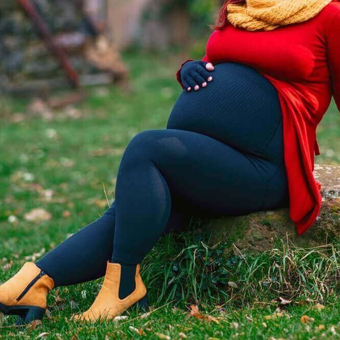 Das Bild zeigt Lipödem-Patientin Kathi Schanz während ihrer Schwangerschaft, die lächelnd auf einem Stein im Garten sitzt. Zur Unterstützung trägt sie ihre VenoTrain curaflow Versorgungen.
