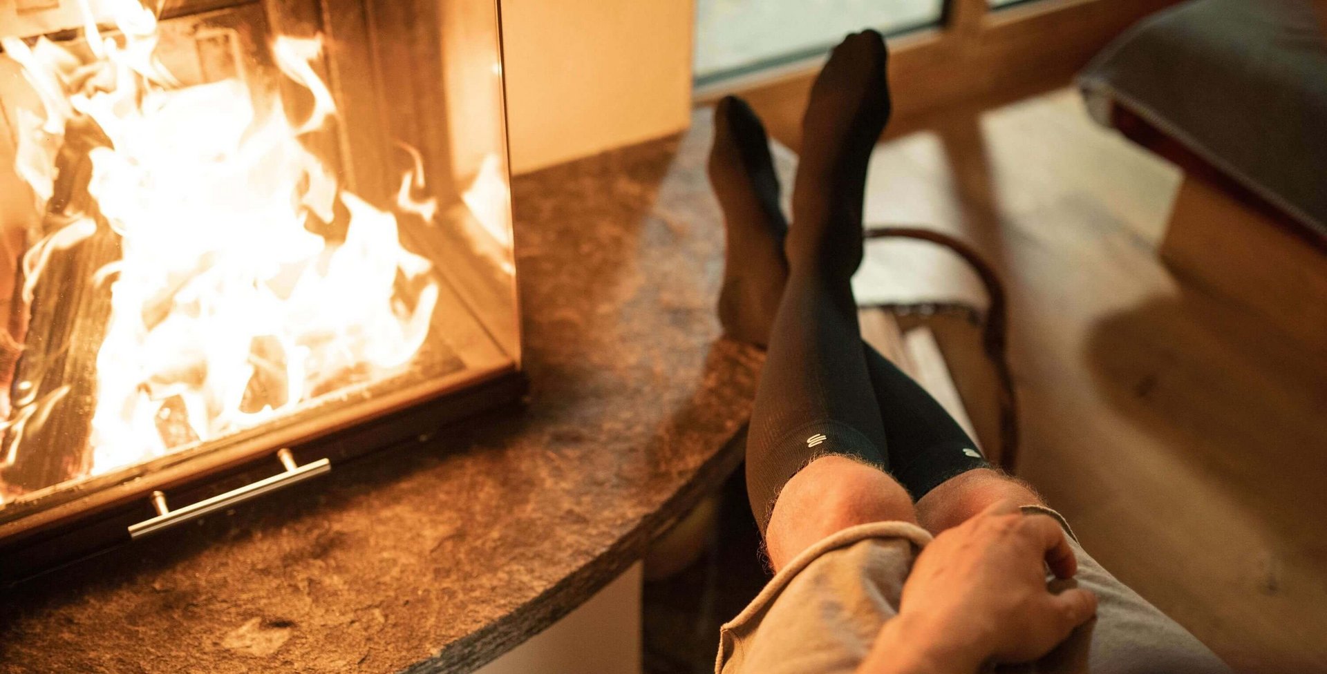 Ein Mann sitzt mit kalten Füßen und Kompressionsstrümpfen vor dem Kamin.