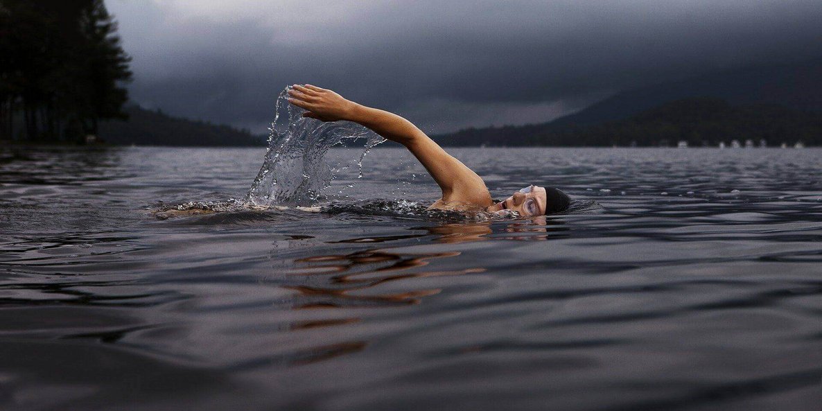 Auf dem Bild krault eine Schwimmerin durch einen See. Schwimmen gilt als eine von Sportart, welche die Gelenke schont.