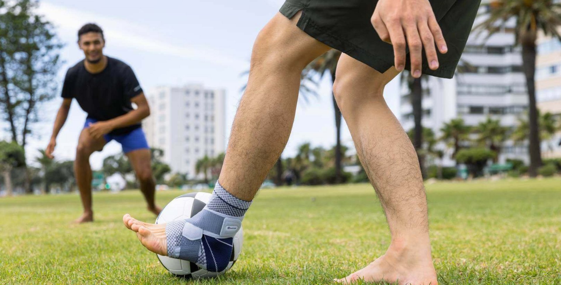 Bildausschnitt zweier Männer beim Fußballspielen im Park. Einer der Männer trägt zur Unterstützung des Sprunggelenks eine MalleoTrain Bandage am linken Bein.