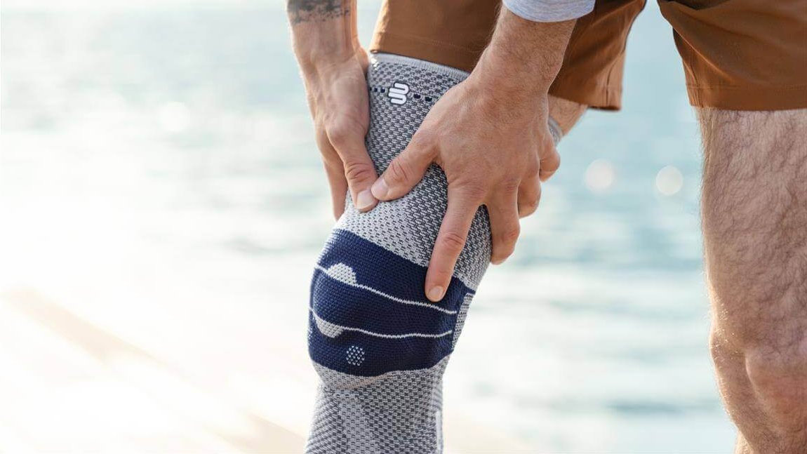 Nahaufnahme der GenuTrain Kniebandage. Die Bandage umschließt das rechte Knie und zeigt ein modernes, funktionales Design. Im Hintergrund ist unscharf ein Gewässer zu erkennen.
