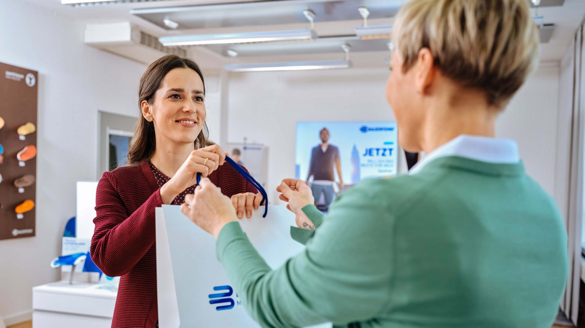 Zu sehen sind zwei Frauen in einer Beratungssituation im Sanitätsfachhandel zu den Hilfsmitteln von Bauerfeind.