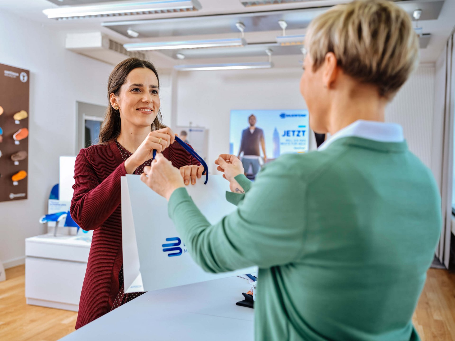 Zu sehen sind zwei Frauen in einer Beratungssituation im Sanitätsfachhandel zu den Hilfsmitteln von Bauerfeind.