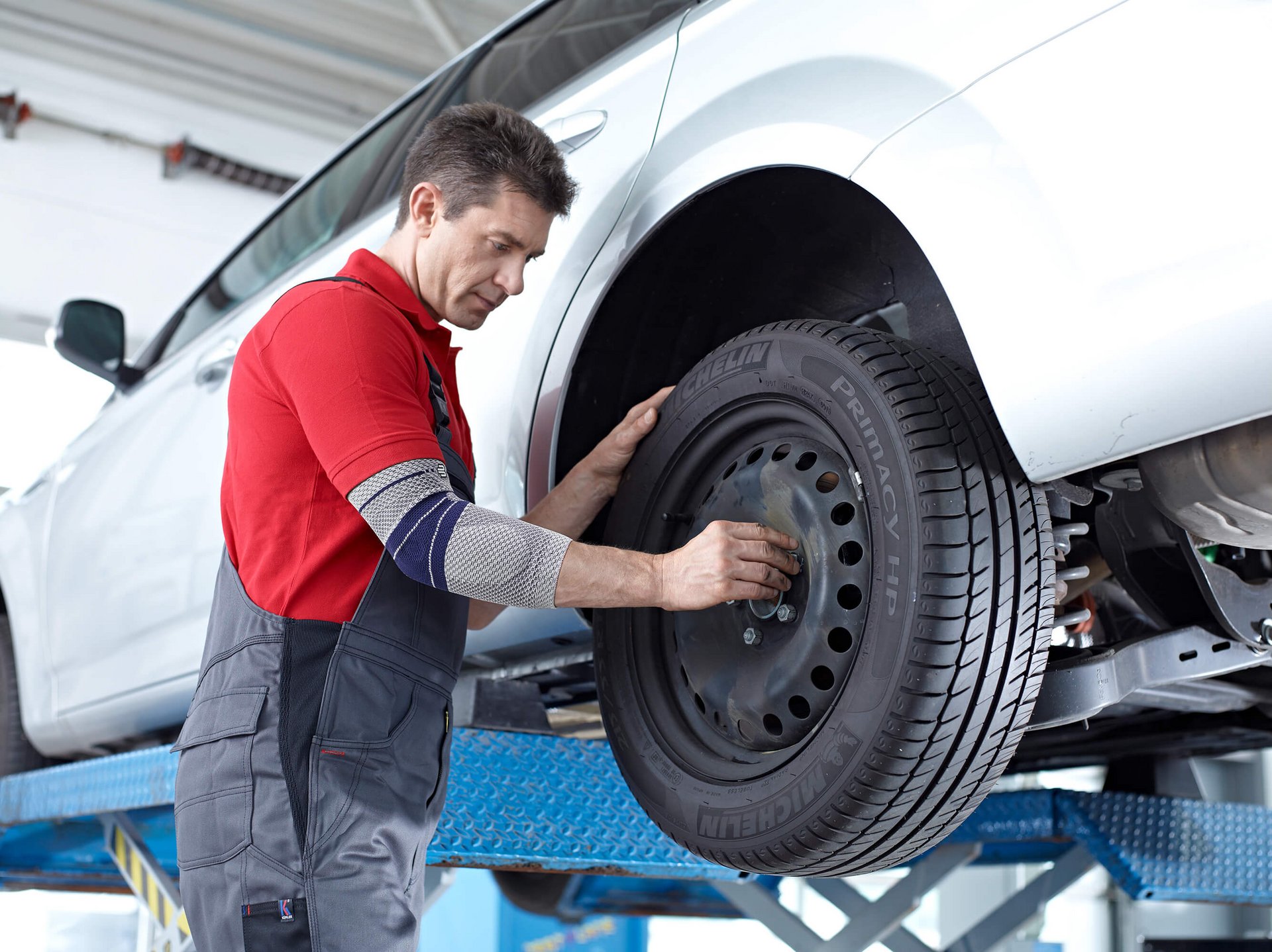 Das Bild zeigt einen Mechaniker in Arbeitskleidung, der einen Autoreifen montiert.Dabei trägt er eine EpiTrain Ellenbogenbandage von Bauerfeind, die bei einem Golferellenbogen Unterstützung und Schmerzlinderung bietet.