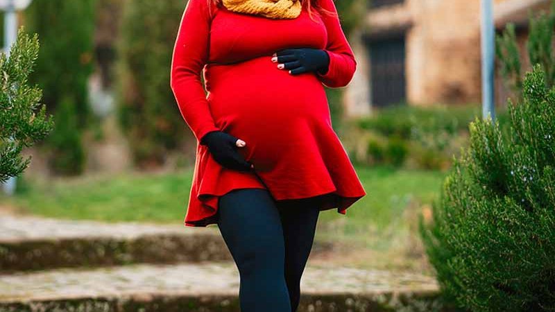 Kathi Schanz in einem roten Kleid und Kompressionsstrumpfhosen spaziert durch einen herbstlichen Garten mit curaflow Kompression.
