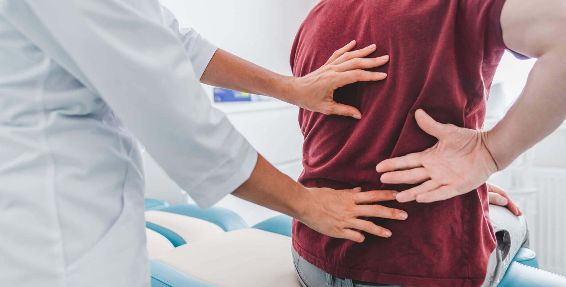 Das Bild zeigt eine Ärztin, die den Rücken und die Hüfte ihres Patienten untersucht, um den Schmerzen auf den Grund zu gehen.
