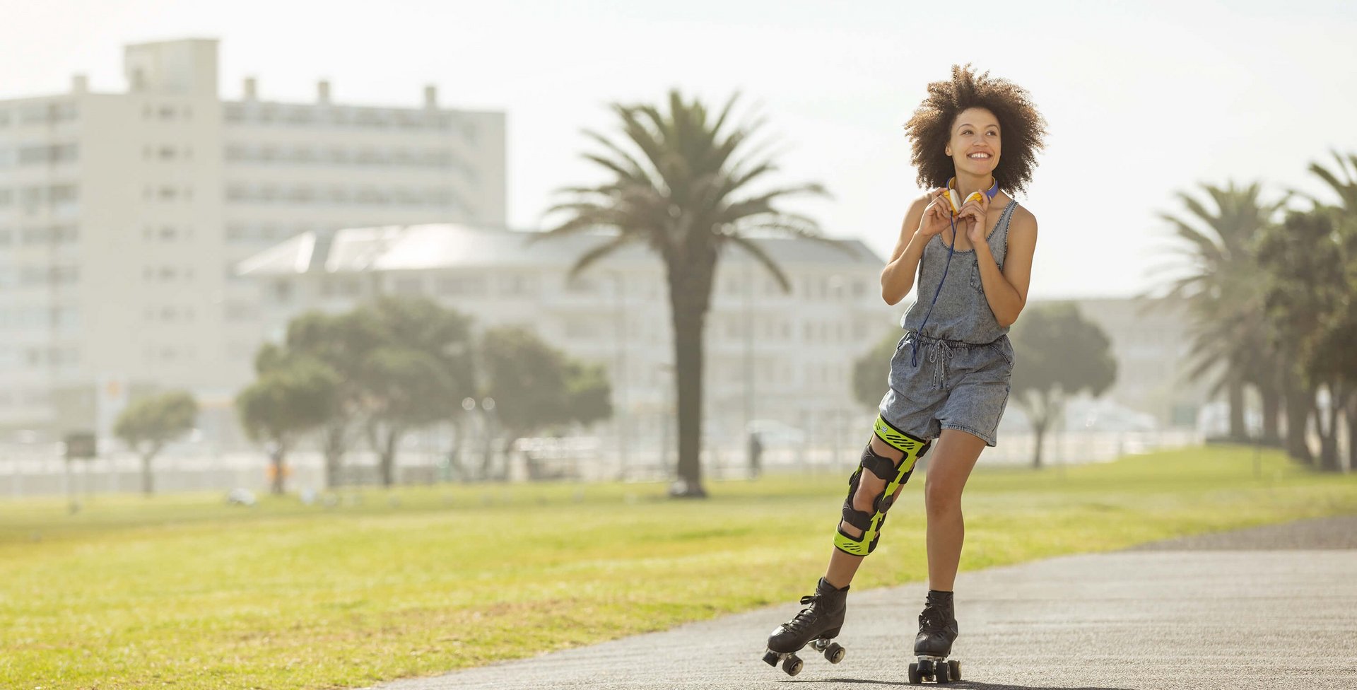 Das Bild zeigt eine lächelnde, junge Frau mit Rollschuhen an einer Strandpromenade. Am Knie trägt sie eine SecuTec Genu. Die Orthese bietet u.a. Unterstützung nach einer Unhappy Triad.  