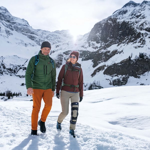 Es sind zwei Personen beim Winterwandern in den Bergen auf dem Bild zu sehen. Eine dieser Personen trägt die Knieorthese SecuTec Genu von Bauerfeind.