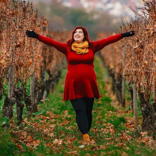 Auf dem Bild ist Kathi Schanz zu sehen, eine Lipödem-Patientin, die während ihrer Schwangerschaft fröhlich in herbstlichen Weinbergen spaziert. Sie trägt ihre VenoTrain curaflow Versorgungen zur Unterstützung.