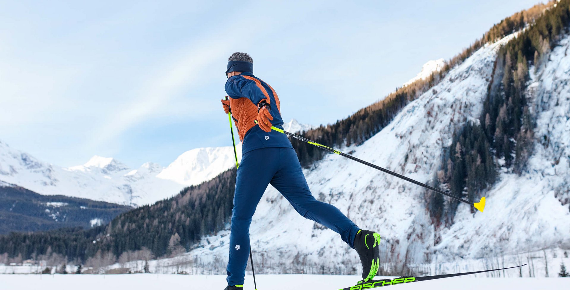 Man erkennt einen Mann beim Langlaufski fahren. Er fährt in einer verschneiten Berglandschaft. Skilanglauf ist eine gelenkschonende Sportart für den Winter.