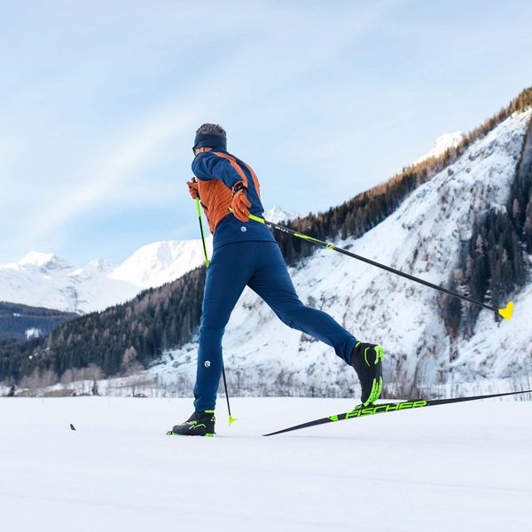 Man erkennt einen Mann beim Langlaufski fahren. Er fährt in einer verschneiten Berglandschaft. Skilanglauf ist eine gelenkschonende Sportart für den Winter.