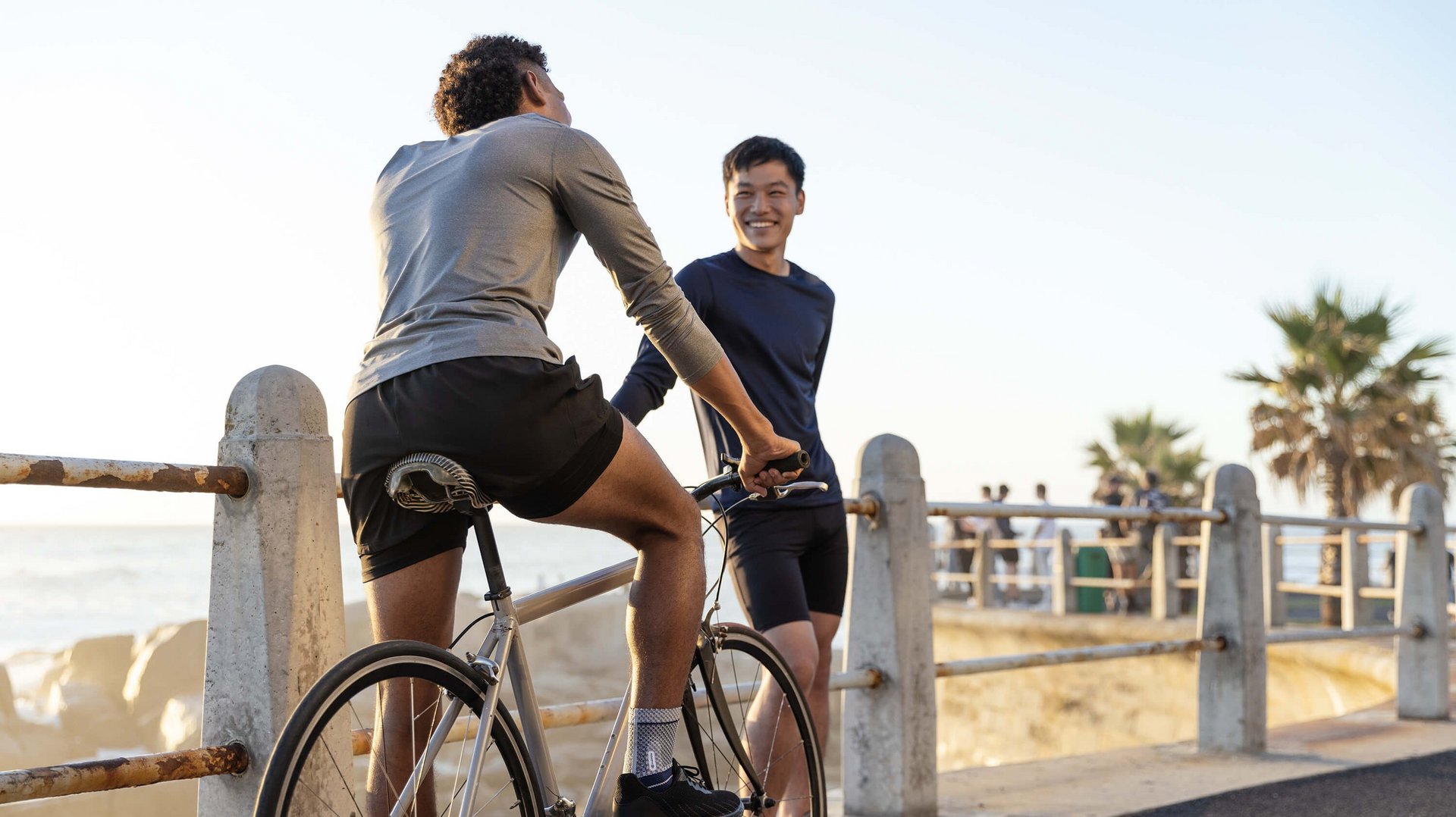 Das Bild zeigt zwei Männer an einer Strandprommenade. Einer von ihnen sitzt auf einem Fahrrad und trägt eine MalleoTrain Bandage zur Unterstützung. Diese kommt u.a. bei einer Arthrose des Sprunggelenks zum Einsatz.
