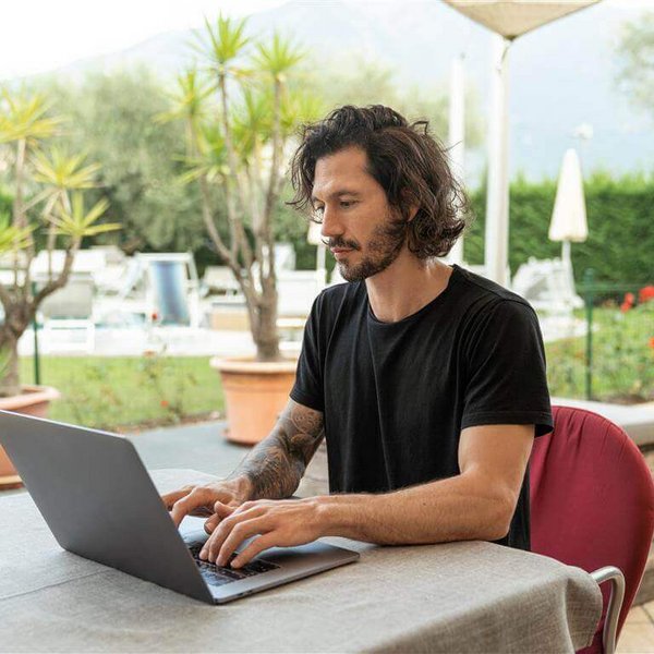 Abgebildet ist ein junger Mann beim Arbeiten an einem Laptop. Monotone Bewegungsabläufe bei der Arbeit können Mausarm-Beschwerden hervorrufen.