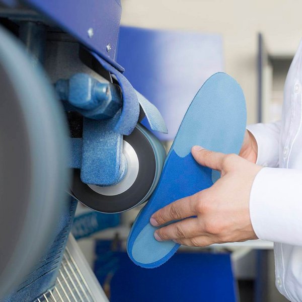 Ein Handwerker bearbeitet eine maßgefertigte orthopädische Einlage mit einer Schleifmaschine, um individuelle Passform und höchsten Tragekomfort zu gewährleisten.