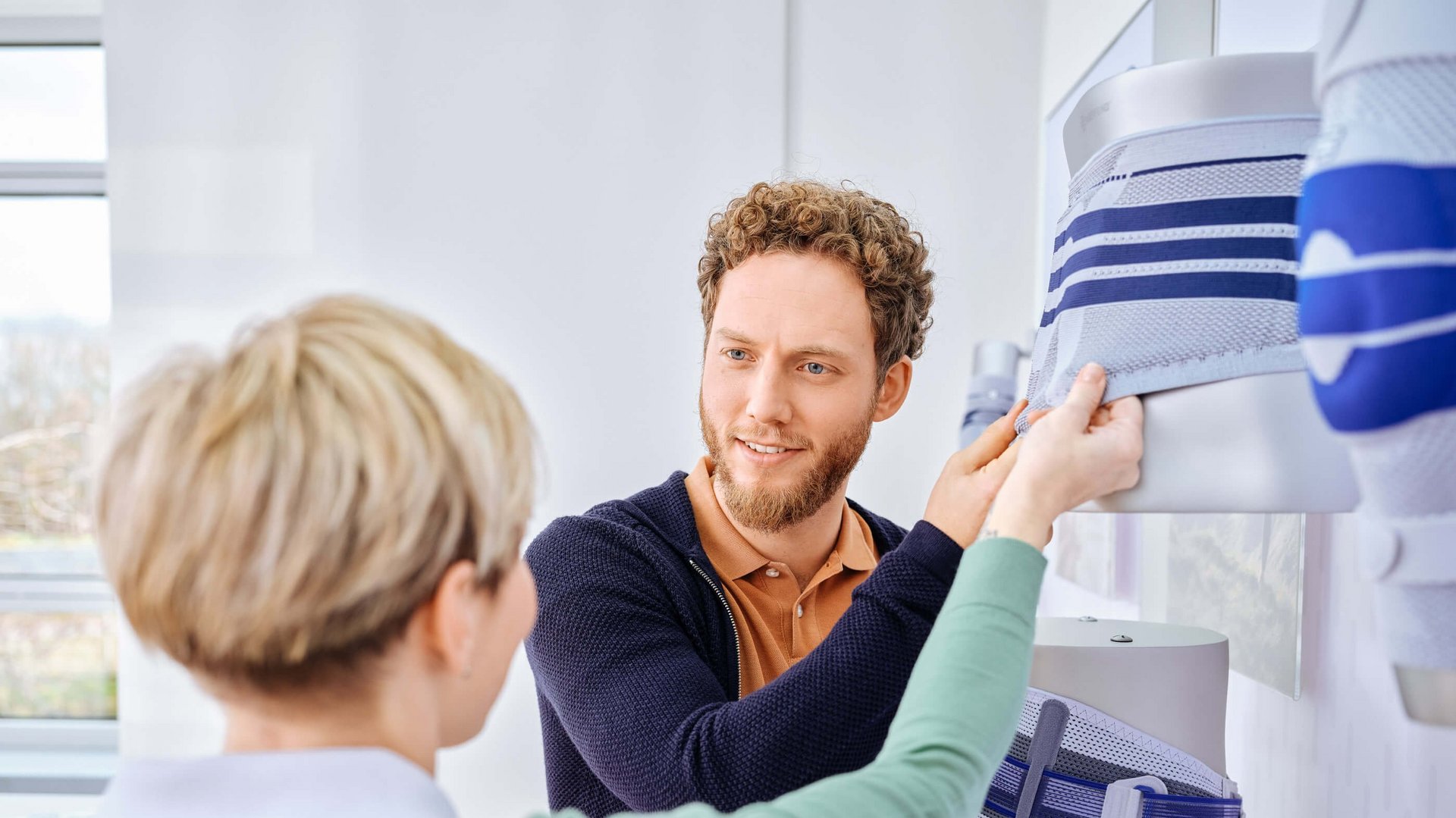 Ein Berater zeigt einer interessierten Patientin die Rückenbandagen von Bauerfeind in einem Showroom.