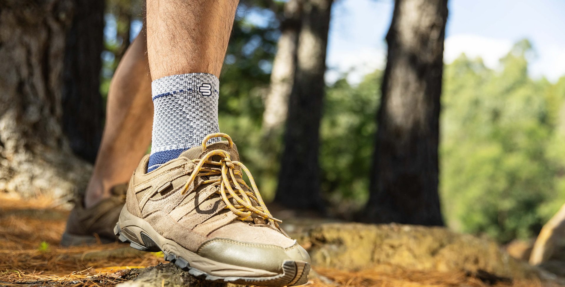 Bildausschnitt eines Wanderers auf einem Waldweg. Neben braunen Wanderschuhen trägt er eine MalleoTrain Bandage, um sein Sprunggelenk zu stabilisieren.