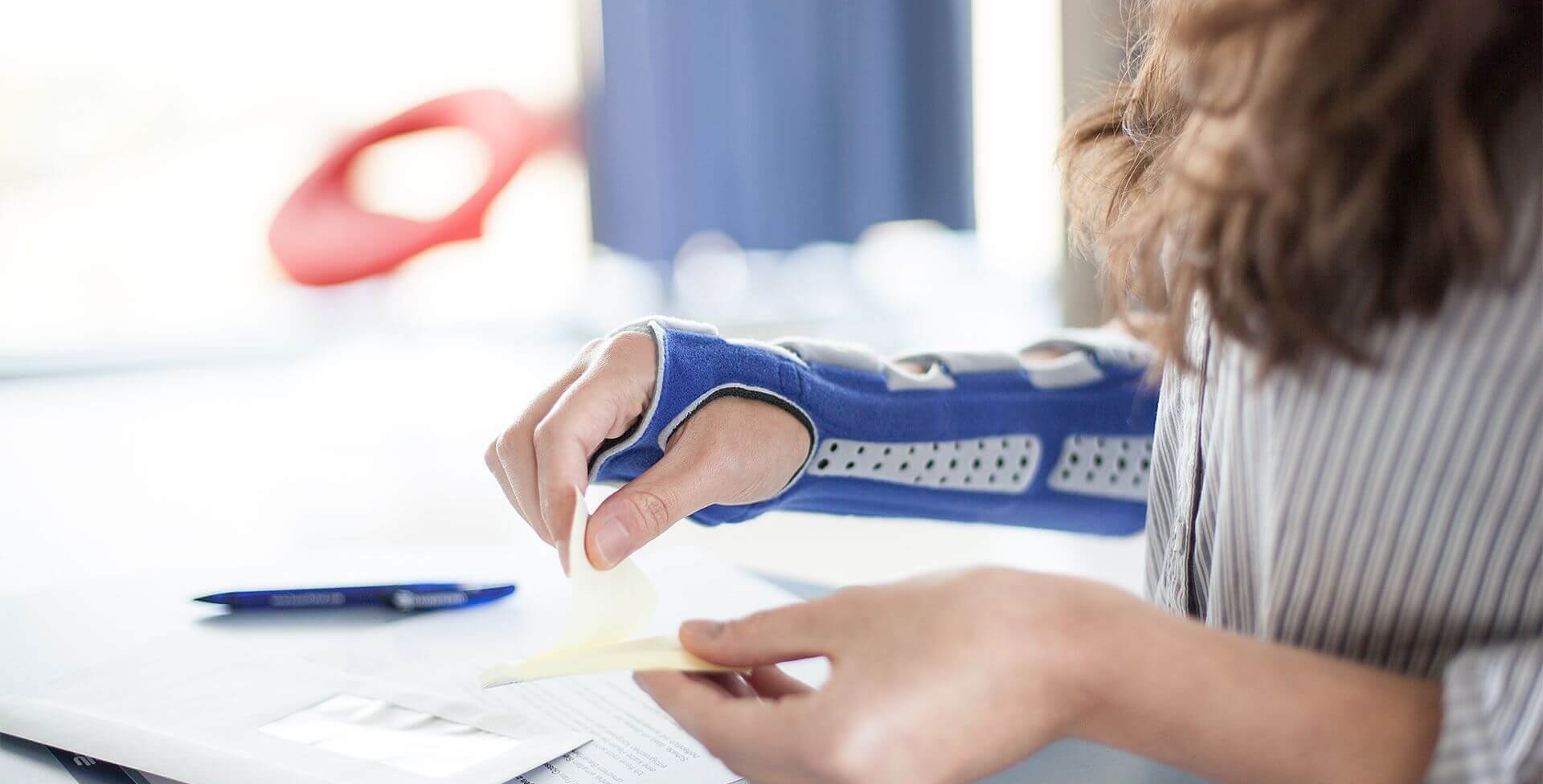 Bildausschnitt einer Frau beim Arbeiten am Schreibtisch. Sie trägt eine ManuLoc Long, eine stablisierende Handgelenksbandage von Bauerfeind, welche u.a. bei einem Karpaltunnelsyndrom angewendet wird.