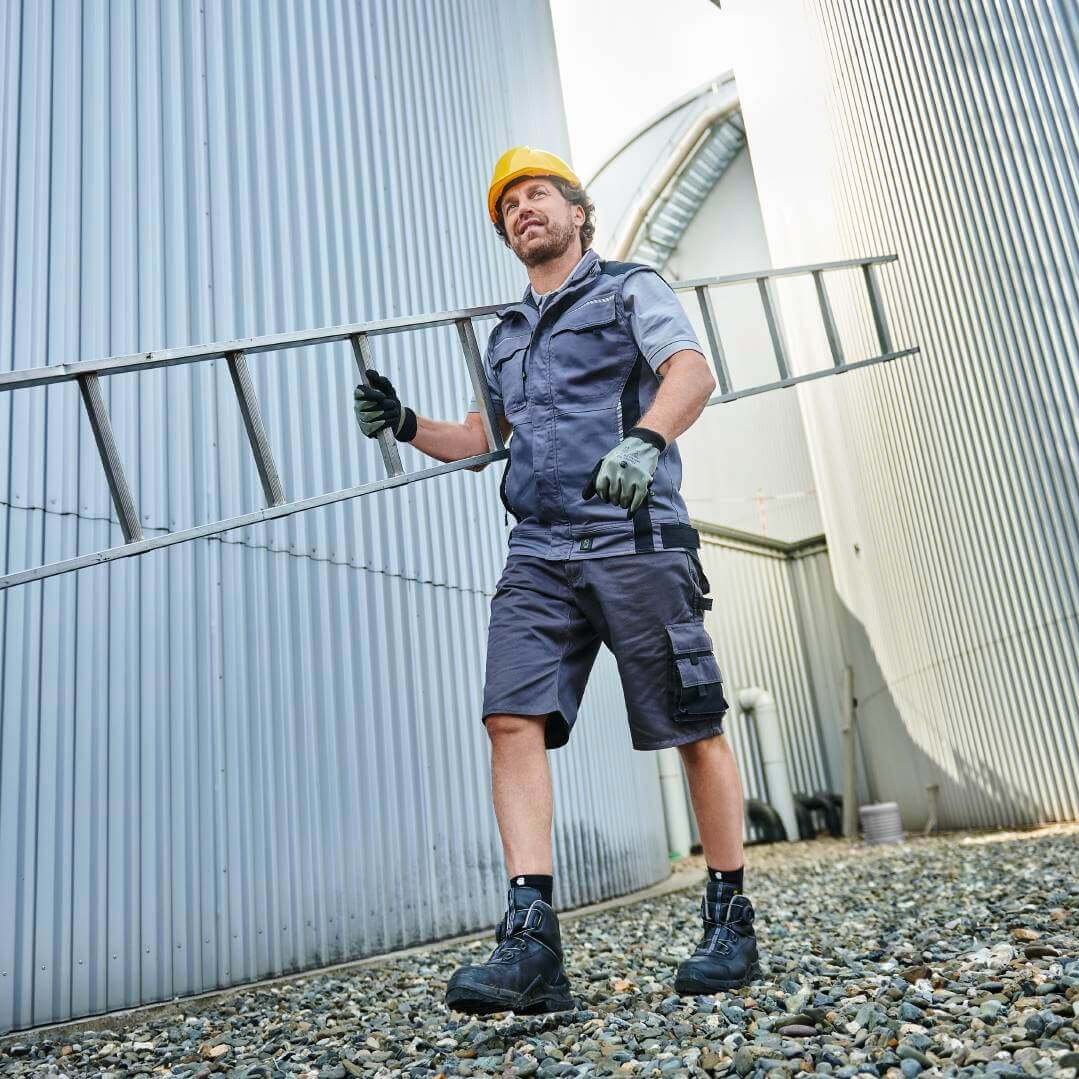 Ein Bauarbeiter trägt eine Leiter zwischen Silos.