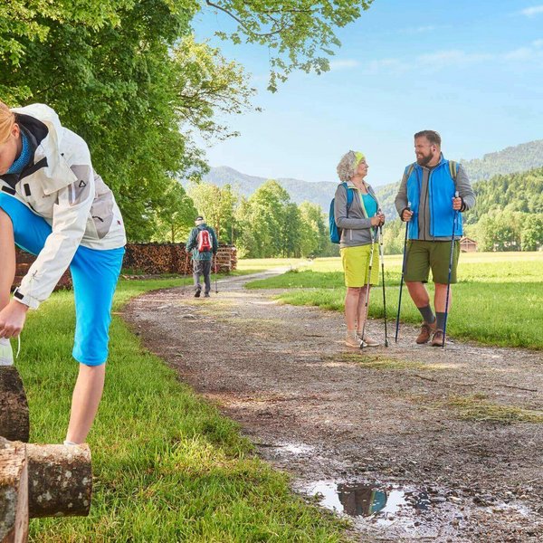 Mehrere Wanderer sind auf einem Wanderweg in den Bergen unterwegs. Im Vordergrund bindet sich eine Frau ihre Schuhe zu. Bauerfeind Einlagen entlasten bei Freizeitaktivitäten Füße, Knie und Hüfte.