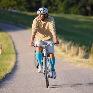 Mann mit Fahrradhelm fährt auf einer sonnigen Landstrasse Fahrrad und trägt auffällige blaue Kompressionsstrümpfe.