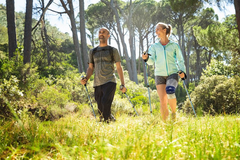 Das Bild zeigt ein Pärchen beim Nordic Walking. Die Frau trägt eine GenuTrain A3 Kniebandage von Bauerfeind gegen arthrosebedingte Schmerzen.