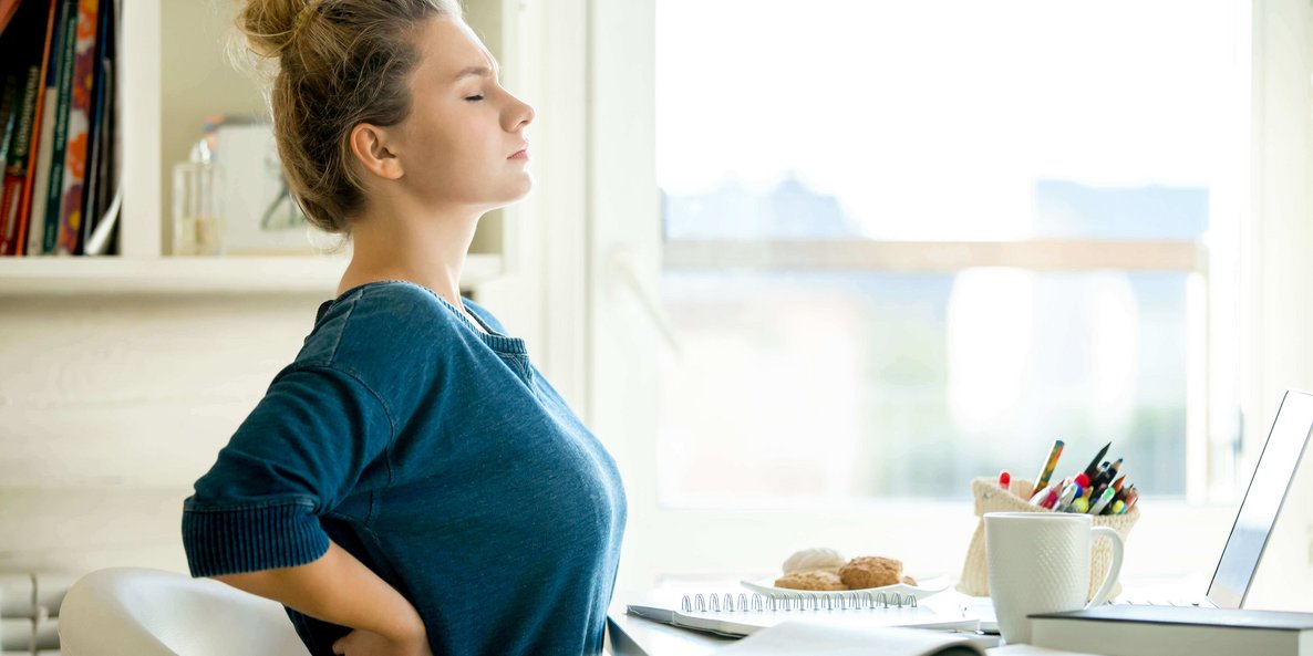 Eine Frau streckt sich an ihrem Homeoffice Arbeitsplatz im Sitzen.