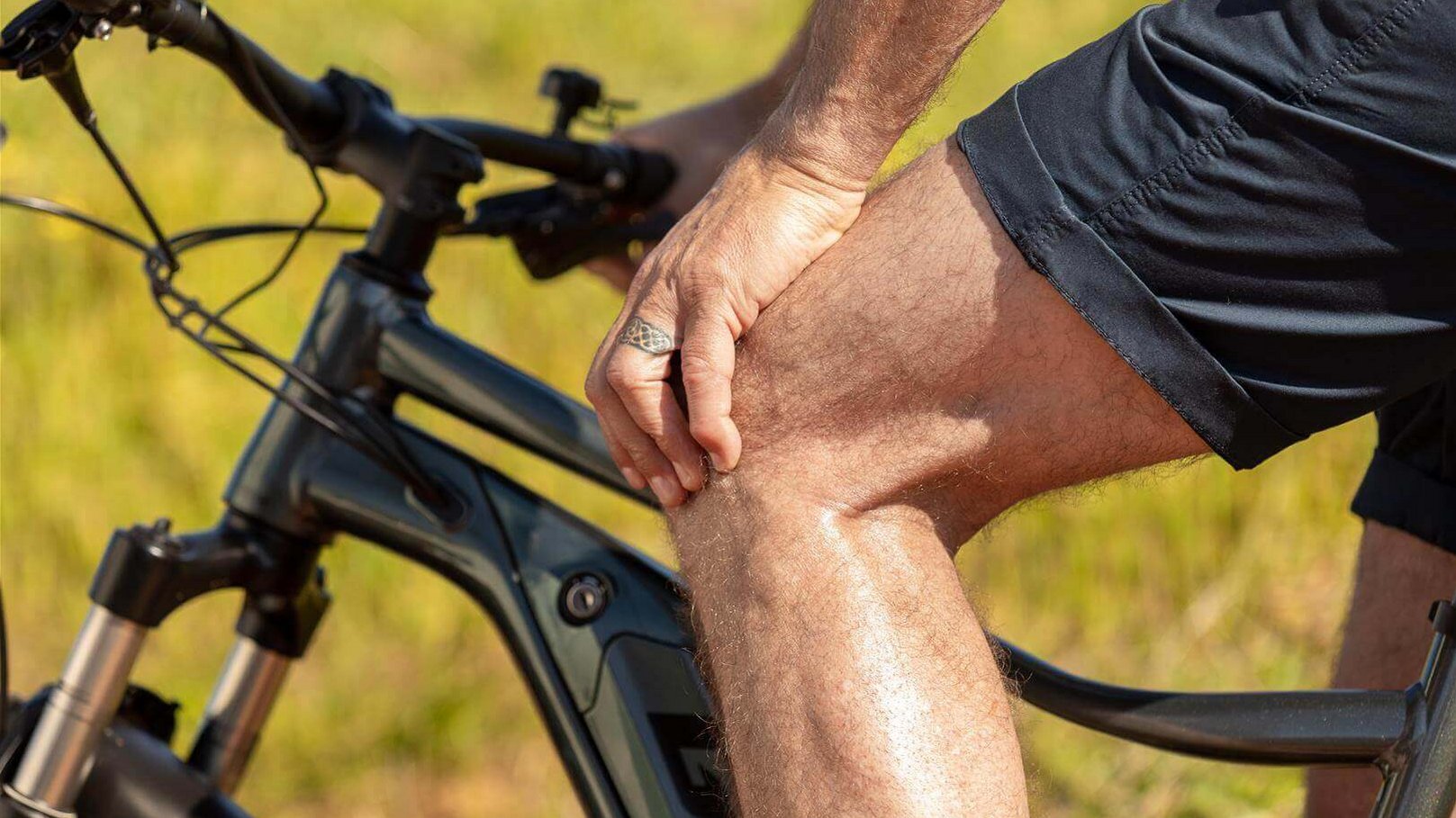 Bildausschnitt eines Radfahres, der sich während einer Pause ans schmerzende Knie fasst. Erfahre, was du gegen Knieschmerzen beim Radfahren tun kannst.