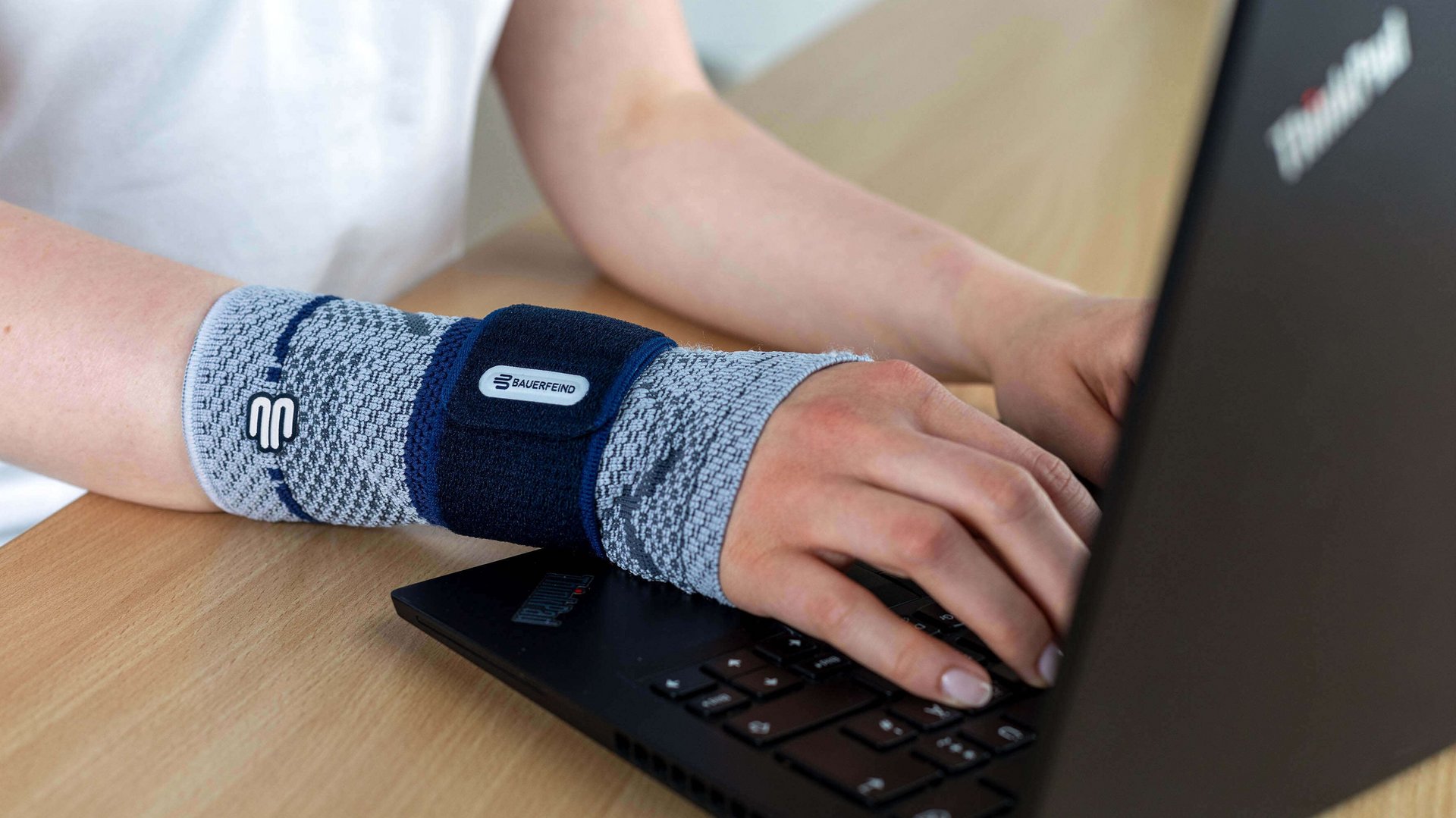 Bildausschnitt einer Frau am Laptop, die am rechten Handgelenk eine ManuTrain Bandage von Bauerfeind trägt. Diese bietet Unterstützung bei Mausarm-Beschwerden.
