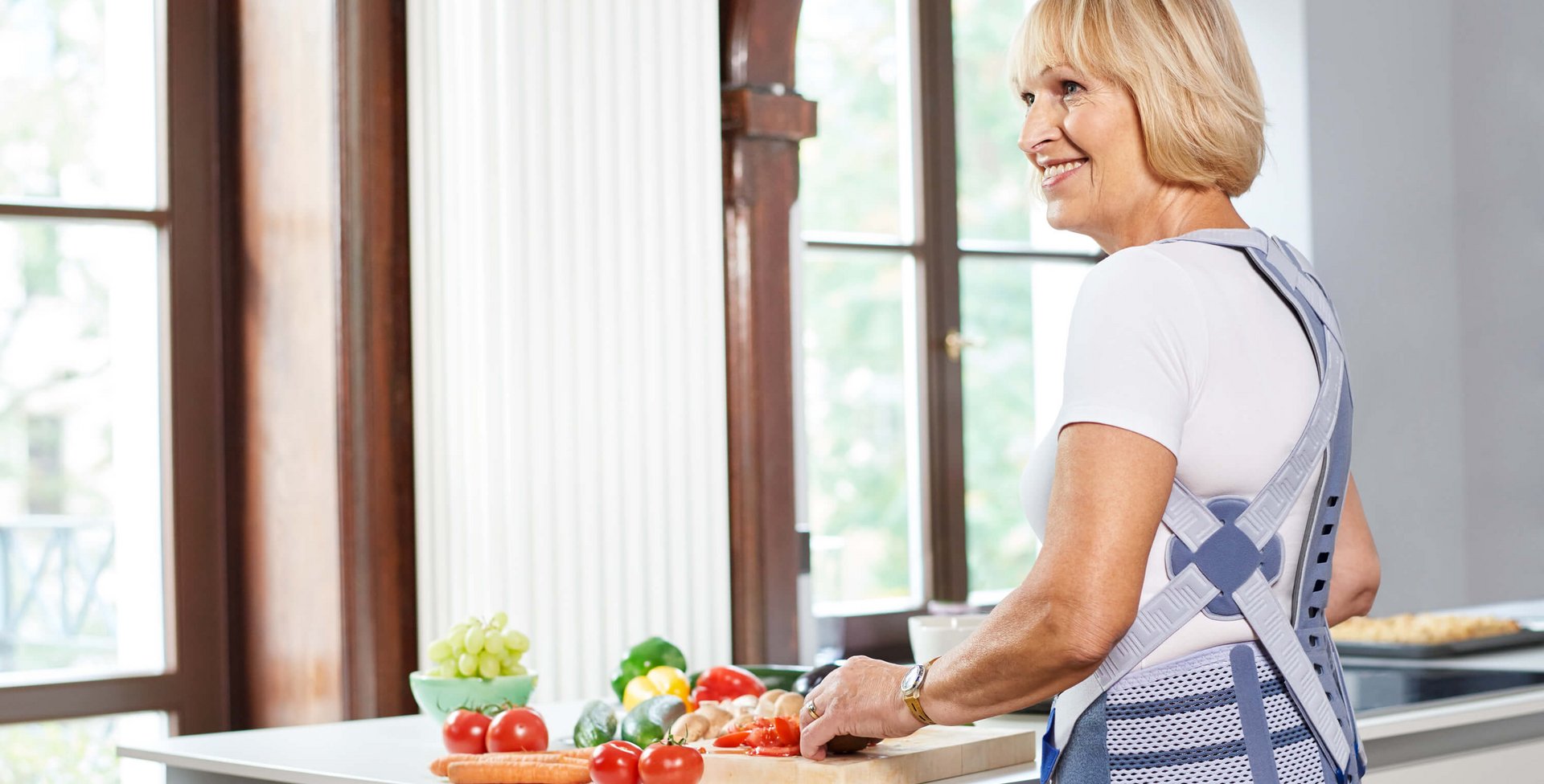 Eine älterer Frau steht in der Küche und bereitet eine Mahlzeit zu. Sie trägt eine Rückenorthese von Bauerfeind.