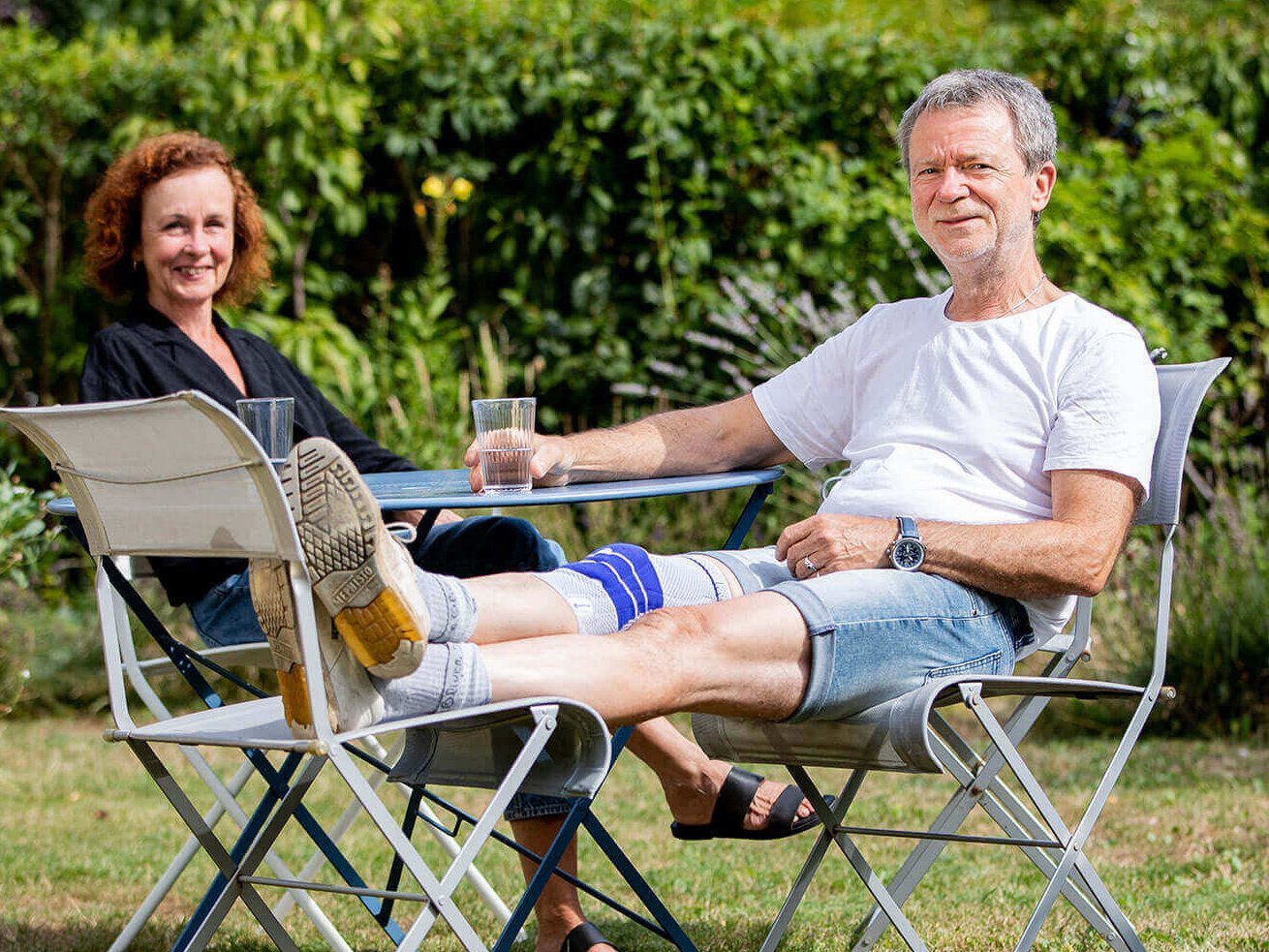 Dieter und Ulli sitzen an einem Tisch in ihrem gepflegten Garten. Dieter trägt eine GenuTrain Kniebandage von Bauerfeind.