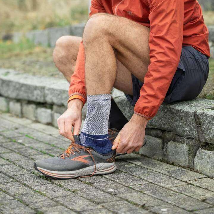 Das Bild zeigt einen jungen Mann im Garten. Ein Hund läuft um seine Beine. Der Mann trägt eine AchilloTrain Sprungelenkbandage von Bauerfeind am rechten Fuß. Diese Bandage entlastet gezielt die Achillessehne.