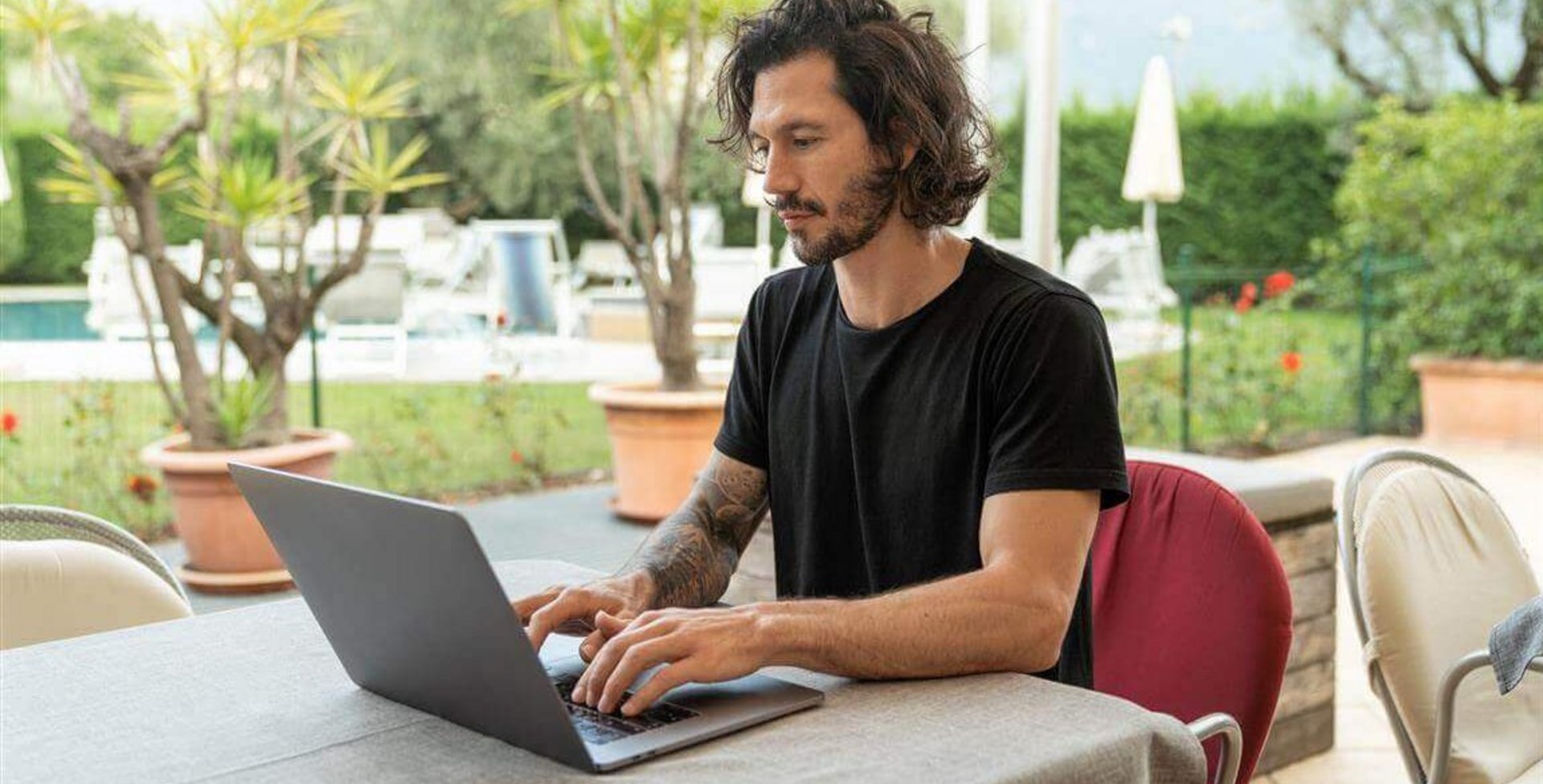 Abgebildet ist ein junger Mann beim Arbeiten an einem Laptop. Monotone Bewegungsabläufe bei der Arbeit können Mausarm-Beschwerden hervorrufen.