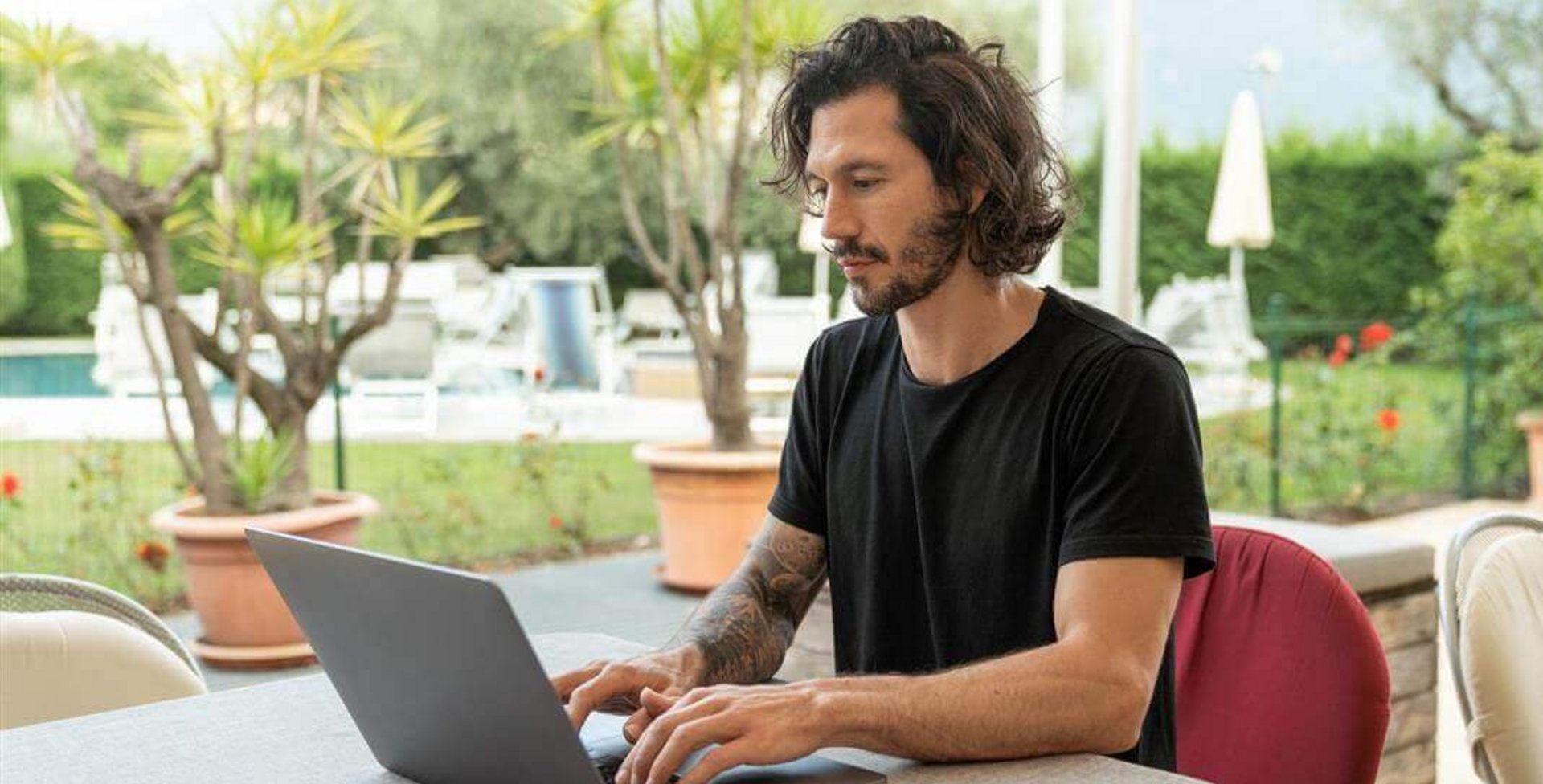 Abgebildet ist ein junger Mann beim Arbeiten an einem Laptop. Monotone Bewegungsabläufe bei der Arbeit können Mausarm-Beschwerden hervorrufen.
