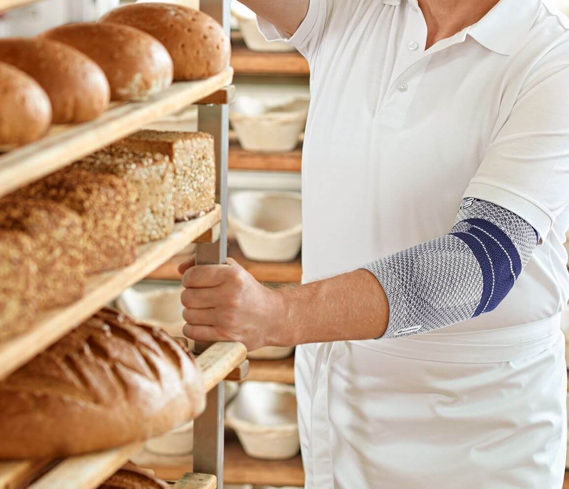 Bildausschnitt eines Bäckers in seiner Backstube. Er trägt eine EpiTrain Ellenbogenmassage von Bauerfeind am linken Arm. Die EpiTrain Bandage lindert Schmerzen im Ellenbogen und verbessert seine Beweglichkeit.