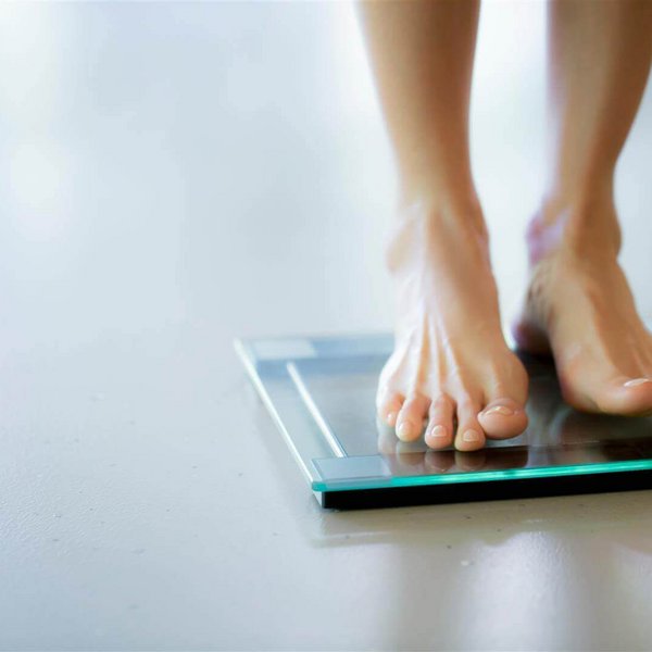 Frauenfüße stehen auf einer digitalen Glaswaage auf hellem Boden.