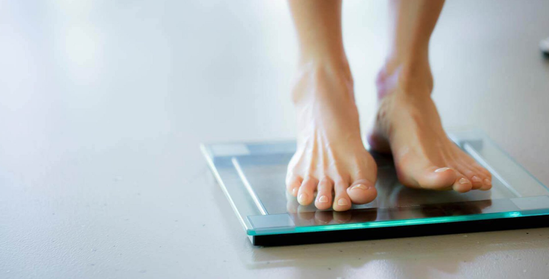 Frauenfüße stehen auf einer digitalen Glaswaage auf hellem Boden.