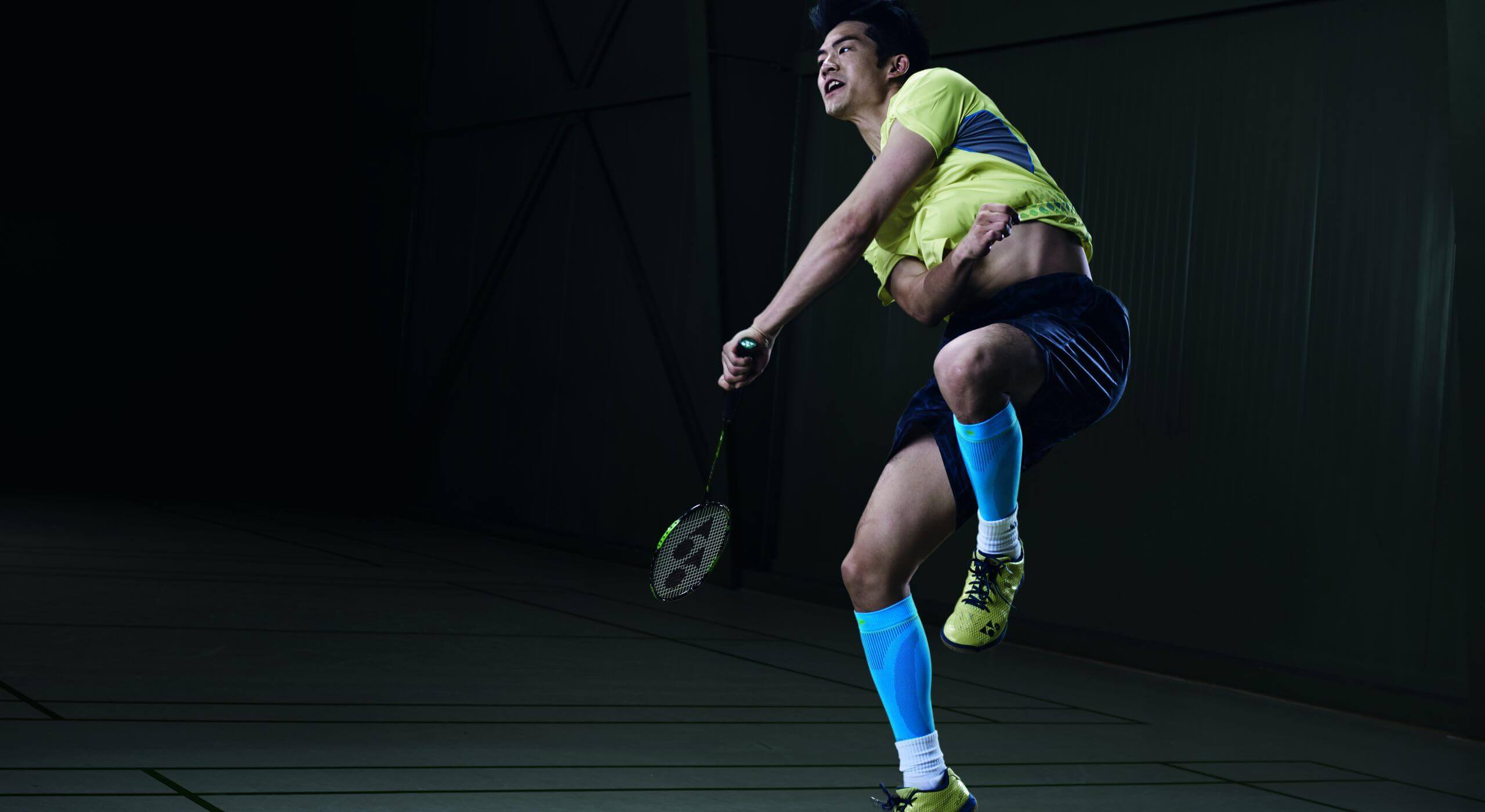 Ein junger Mann mit Badmintonschläger in der Hand ist in einer Sprungbewegung. Er trägt Sports Compression Sleeves Lower Leg von Bauerfeind in der Farbe rivera. Das sind Wadenstulpen zur Kompression des Unterschenkels beim Sport.
