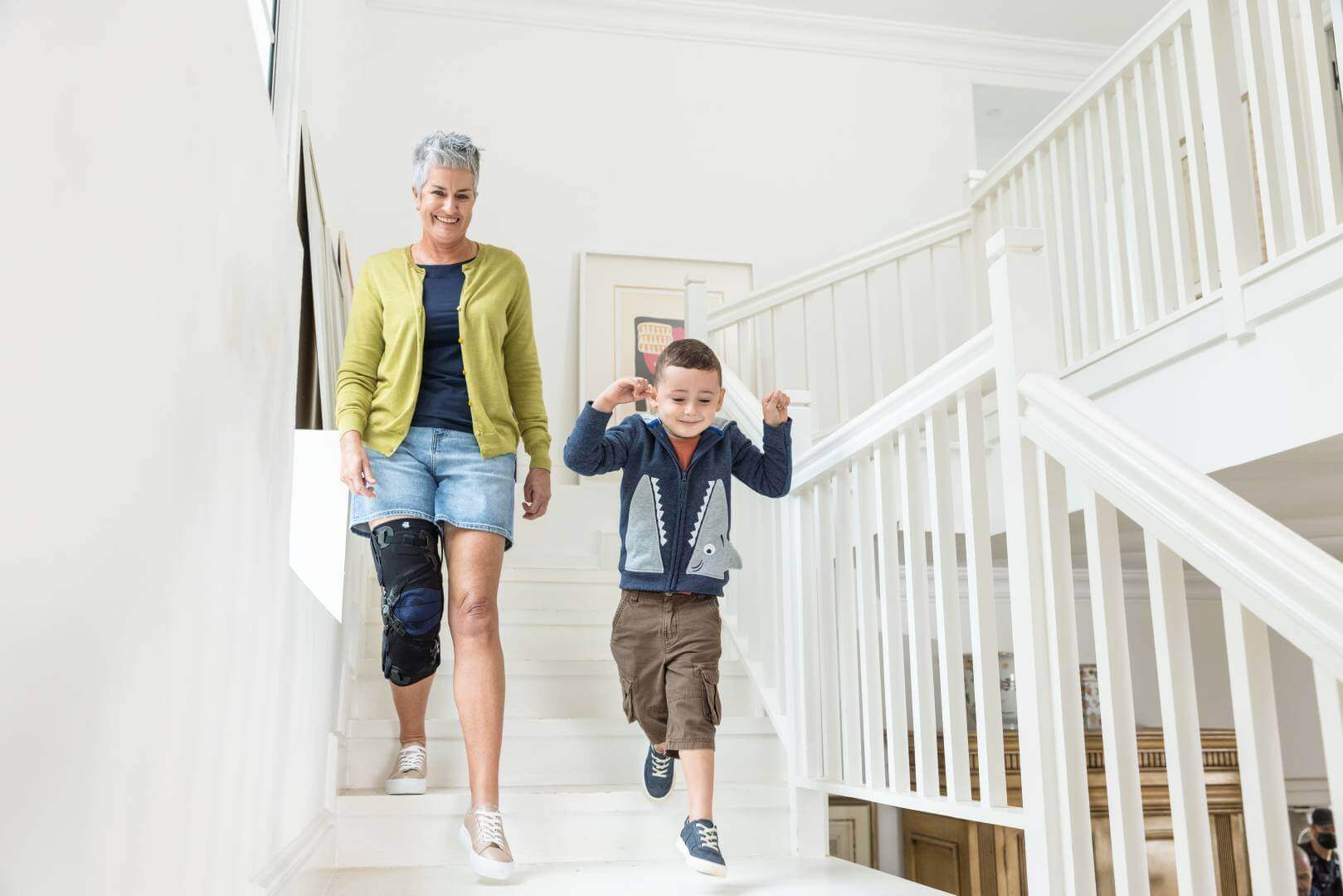 Das Bild zeigt eine Dame mit ihrem Enkel beim Herunterlaufen einer Treppe. Zur Unterstützung ihres Knies trägt die Frau eine Gonarthrose-Orthese von Bauerfeind, die GenuTrain OA.