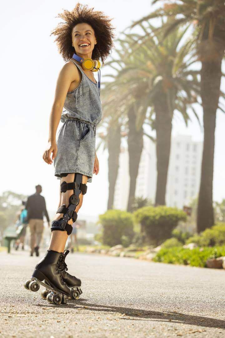 Das Bild zeigt eine lächelnde, junge Frau mit Rollschuhen an einer Strandpromenade. Am Knie trägt sie eine SecuTec Genu. Die Orthese bietet u.a. Unterstützung nach einem Kreuzbandriss.  