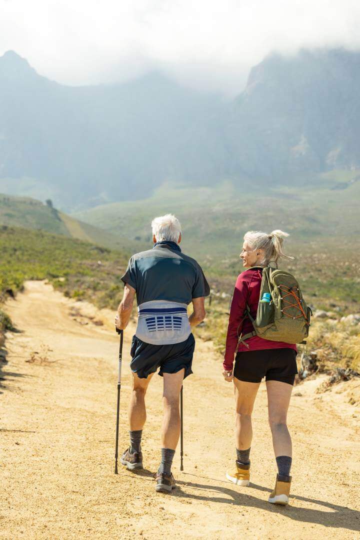 Ein älteres Paar ist am Wandern in den Bergen. Der Mann trägt eine LumboLoc Rückenorthese von Bauerfeind.