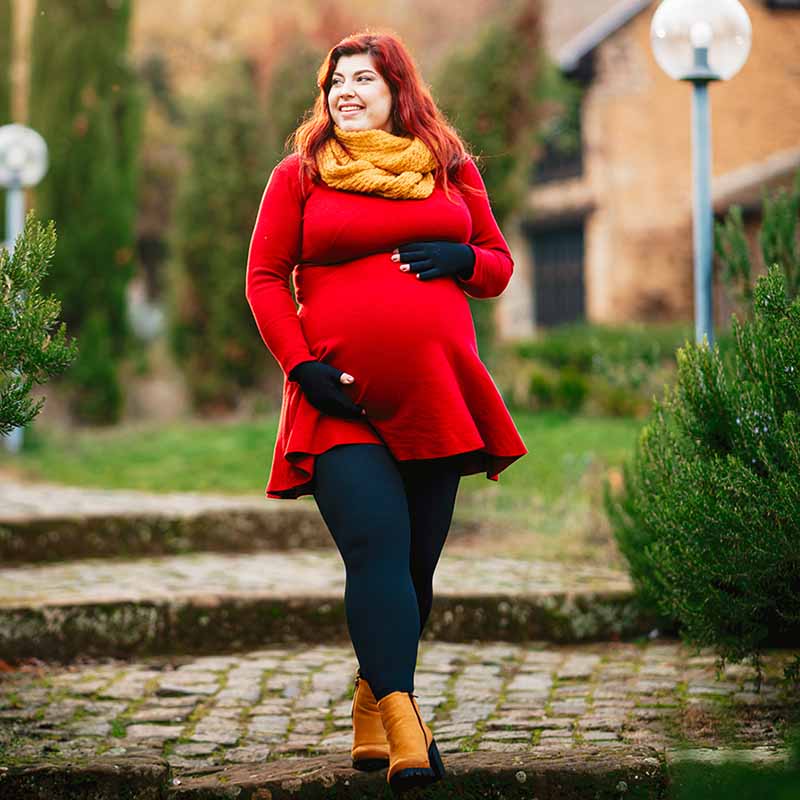 Kathi Schanz in einem roten Kleid und Kompressionsstrumpfhosen spaziert durch einen herbstlichen Garten mit curaflow Kompression.