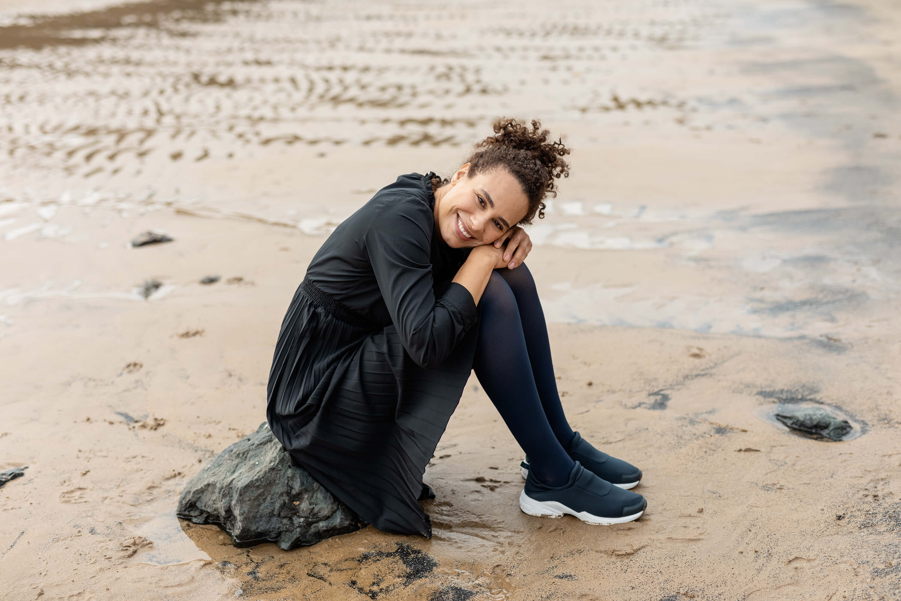 Das Bild zeigt eine Frau die auf einem kleinen Felsen am Strand sitzt. Sie trägt VenoTrain soft Kompressionsstrümpfe von Bauerfeind.