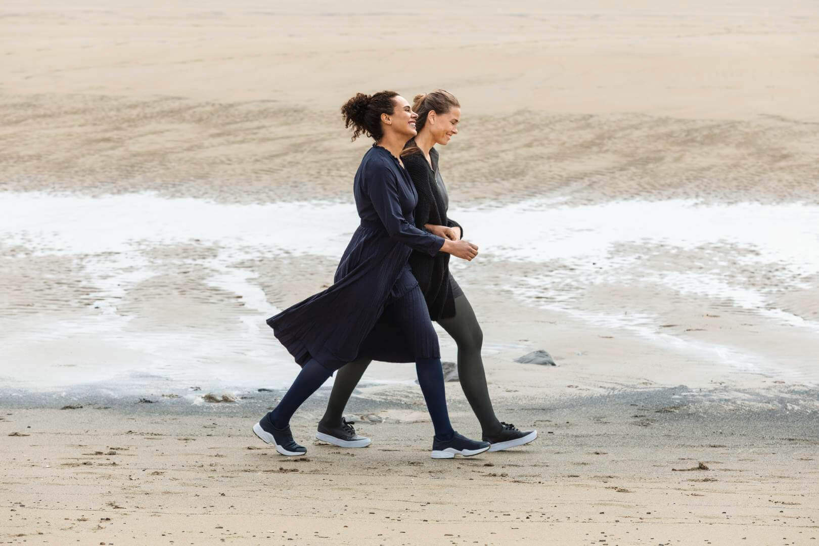 Das Bild zeigt zwei Frauen die am Strand entlang spazieren. Beide tragen VenuTrain soft Kompressionsstrümpfe von Bauerfeind.